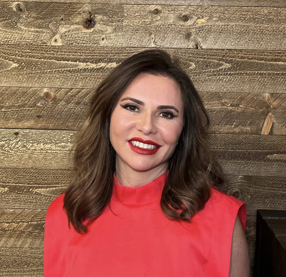 A woman in a red top standing next to a wooden wall.